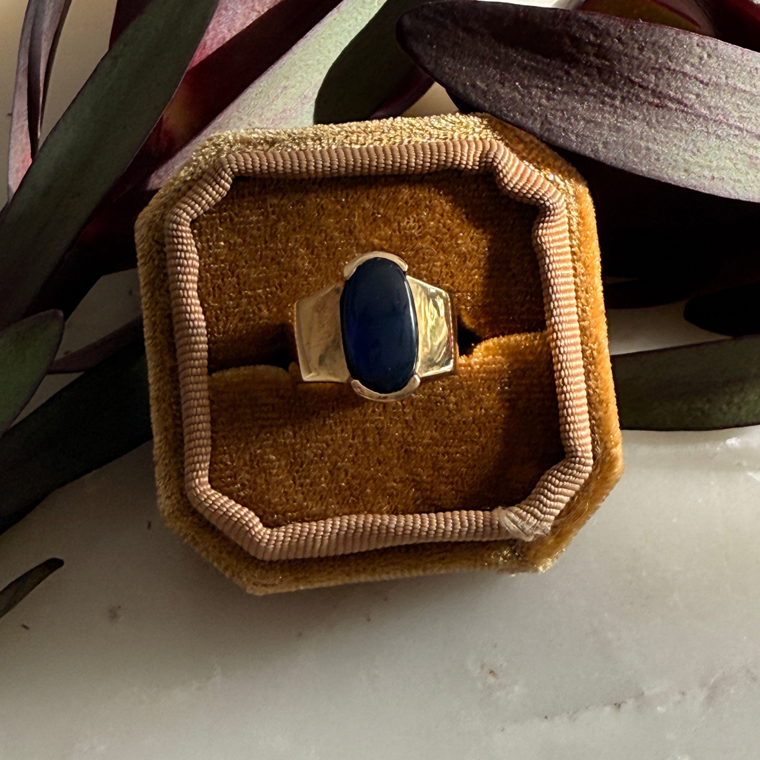 Ring with black opal stone in a brown box on a white surface