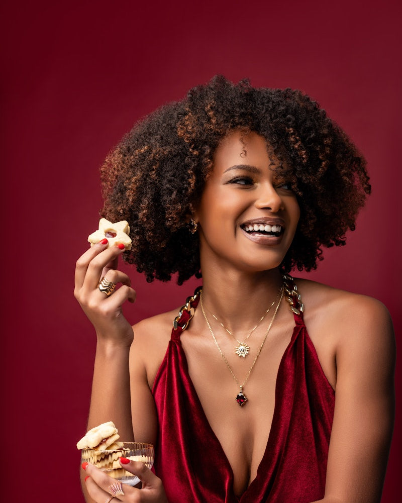 Woman in a red dress holding a glass and a cookie against a red background