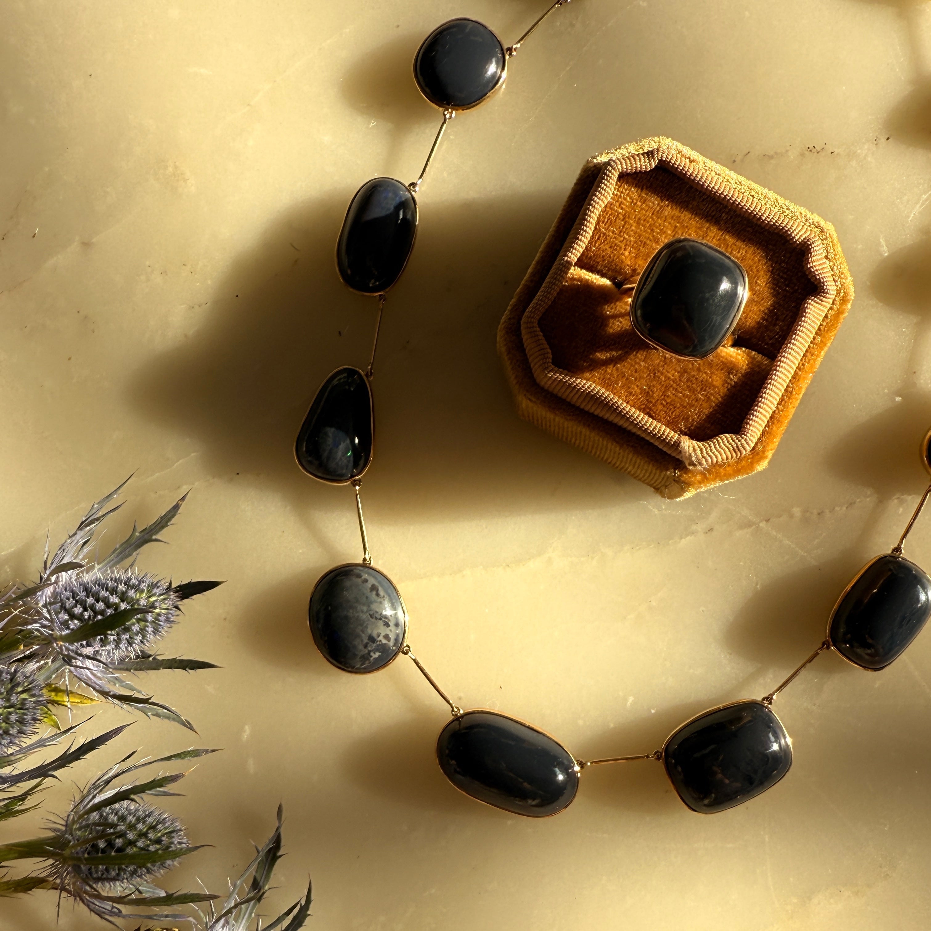 Necklace with black stones on a beige surface with dried flowers