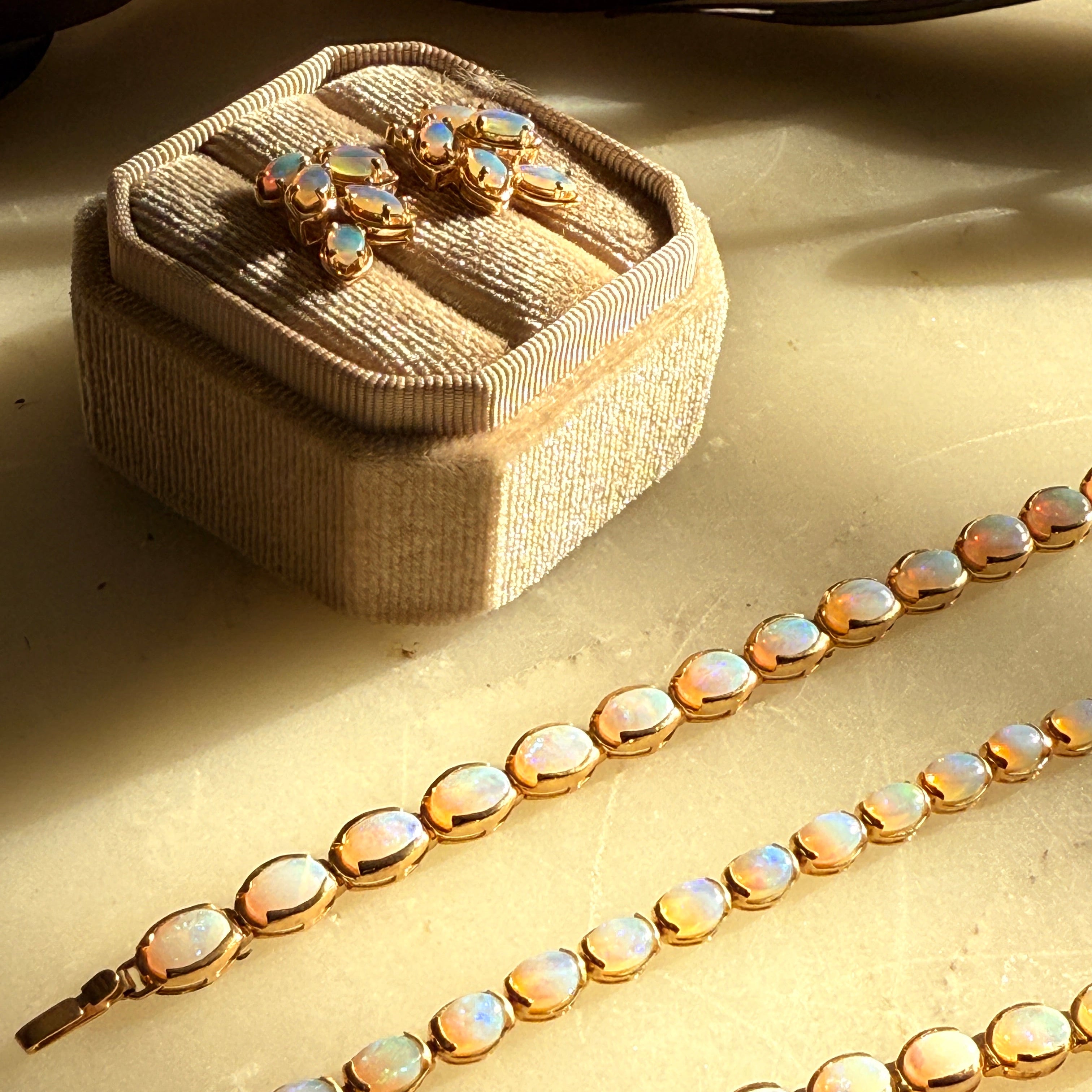 Opal necklace and earrings on a textured surface with a jewelry box.